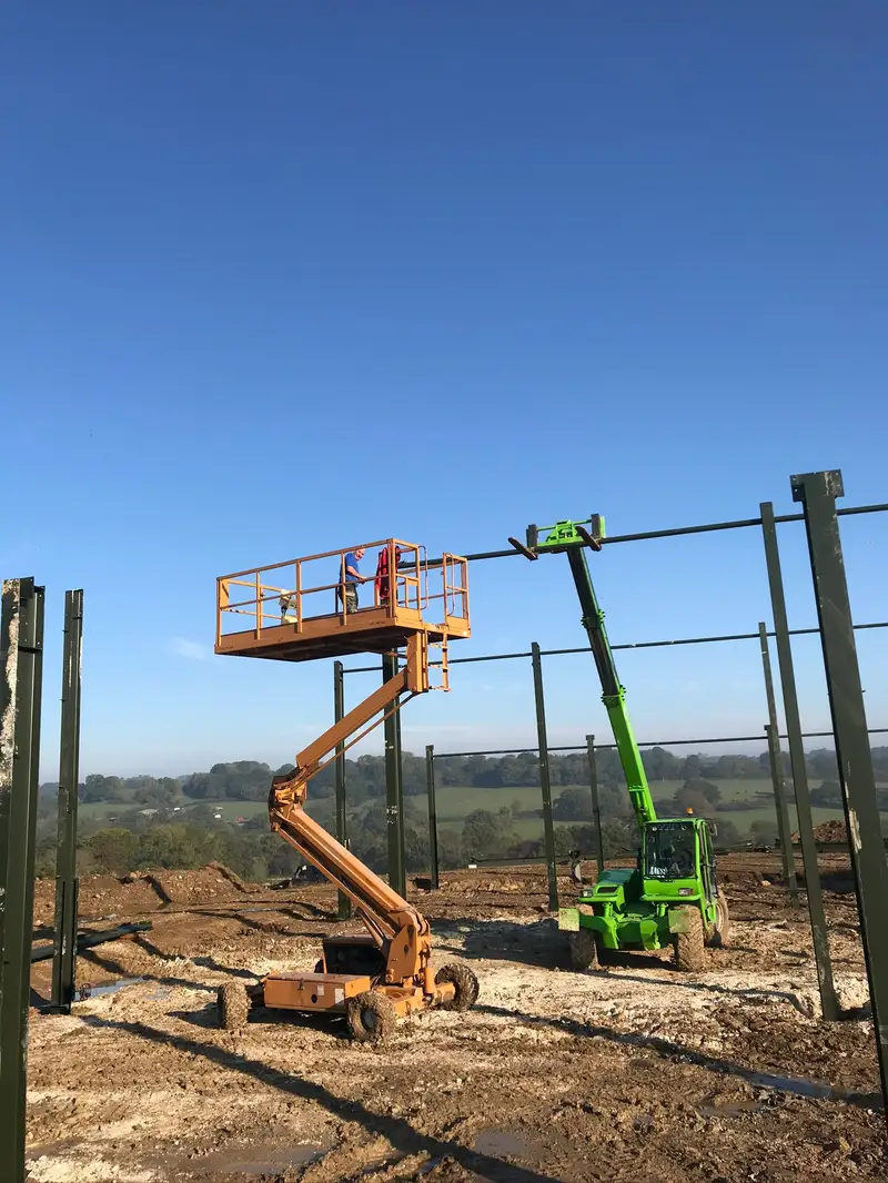 Steel frame erection in progress with cherry picker and telehandler